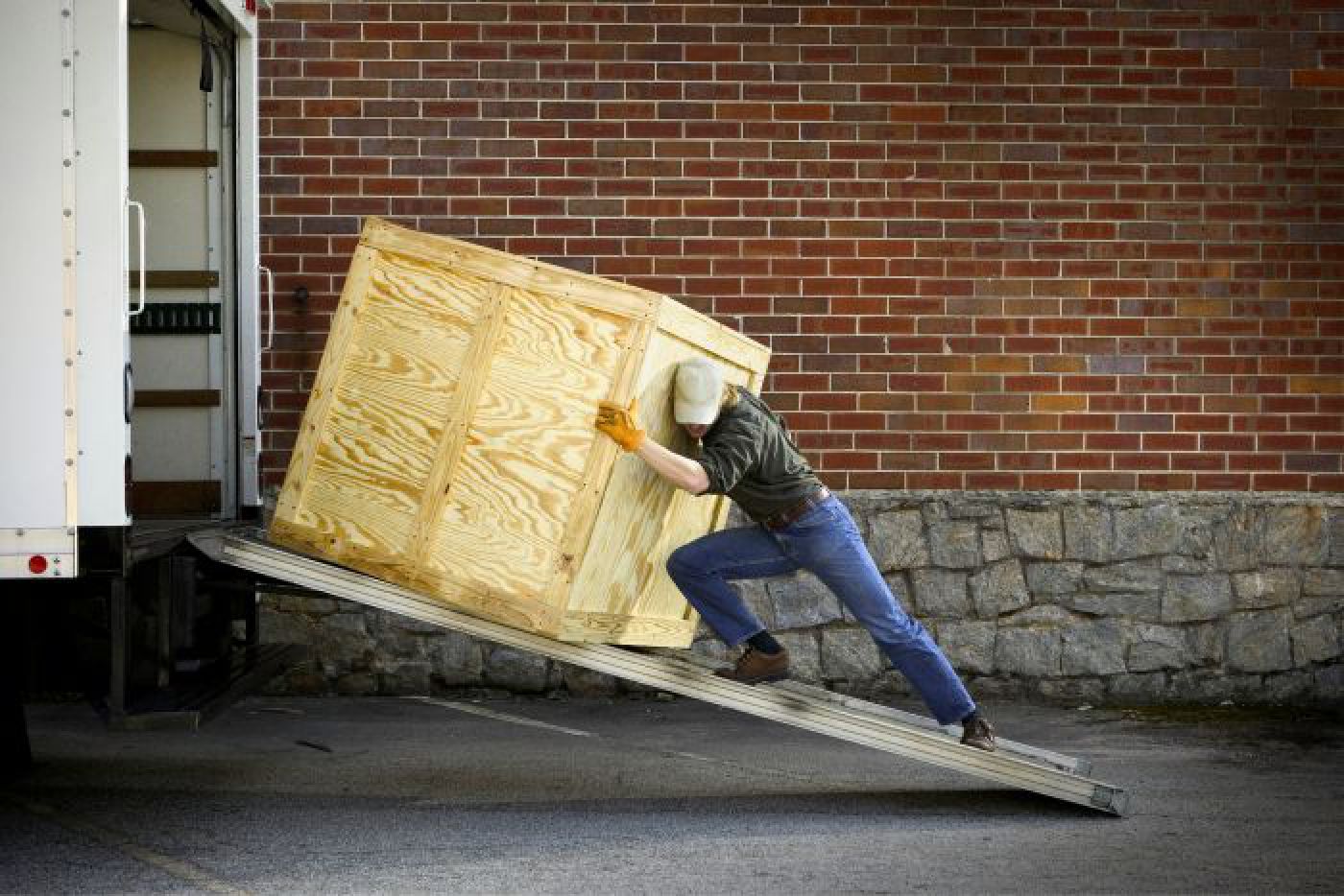 Man loading a wooden shipping container the hard way Man pushing large wooden box up ramp into box truck